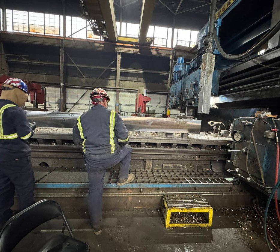 Worker adjusting coolant nozzle on a lathe turning a large steel cylinder