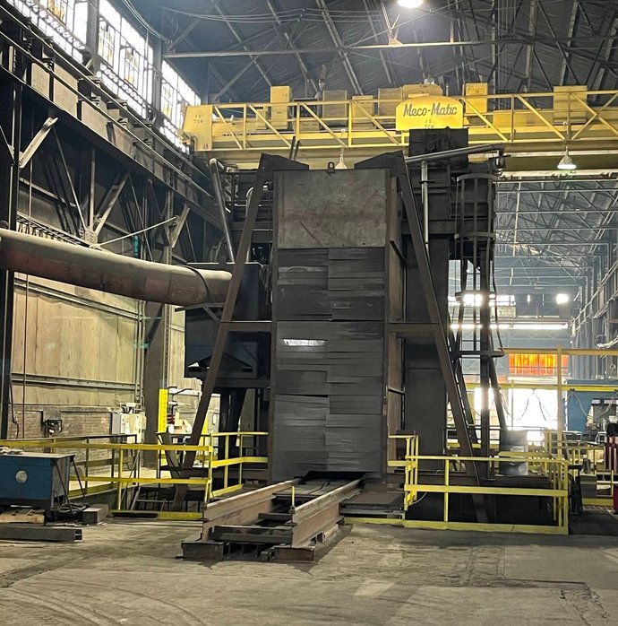 Large stacked steel plates positioned beneath a Meco-Matic overhead crane