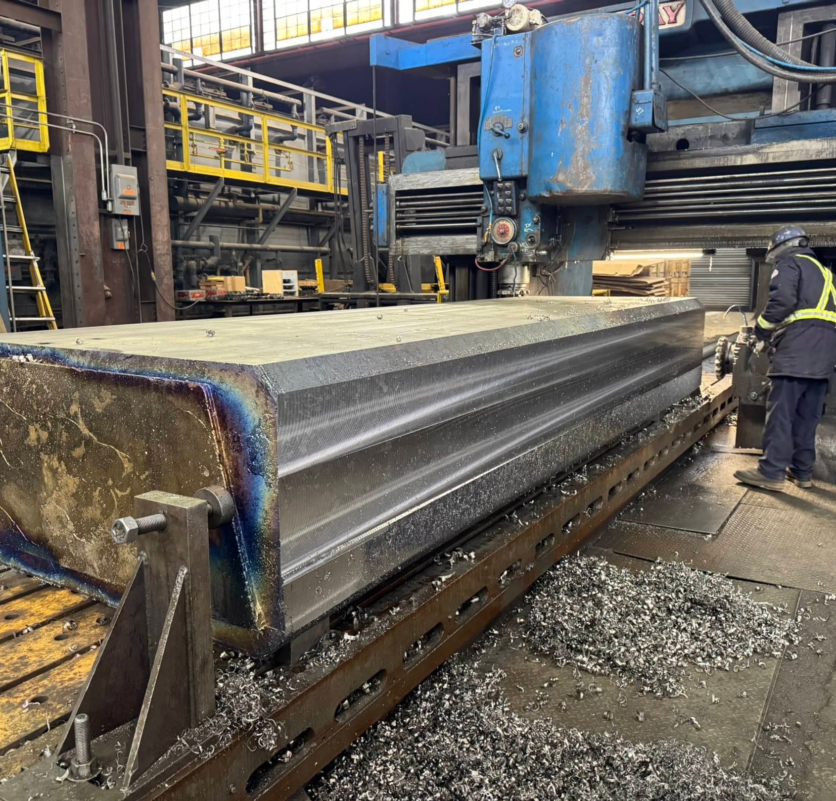 Worker operating a large milling machine cutting a steel workpiece